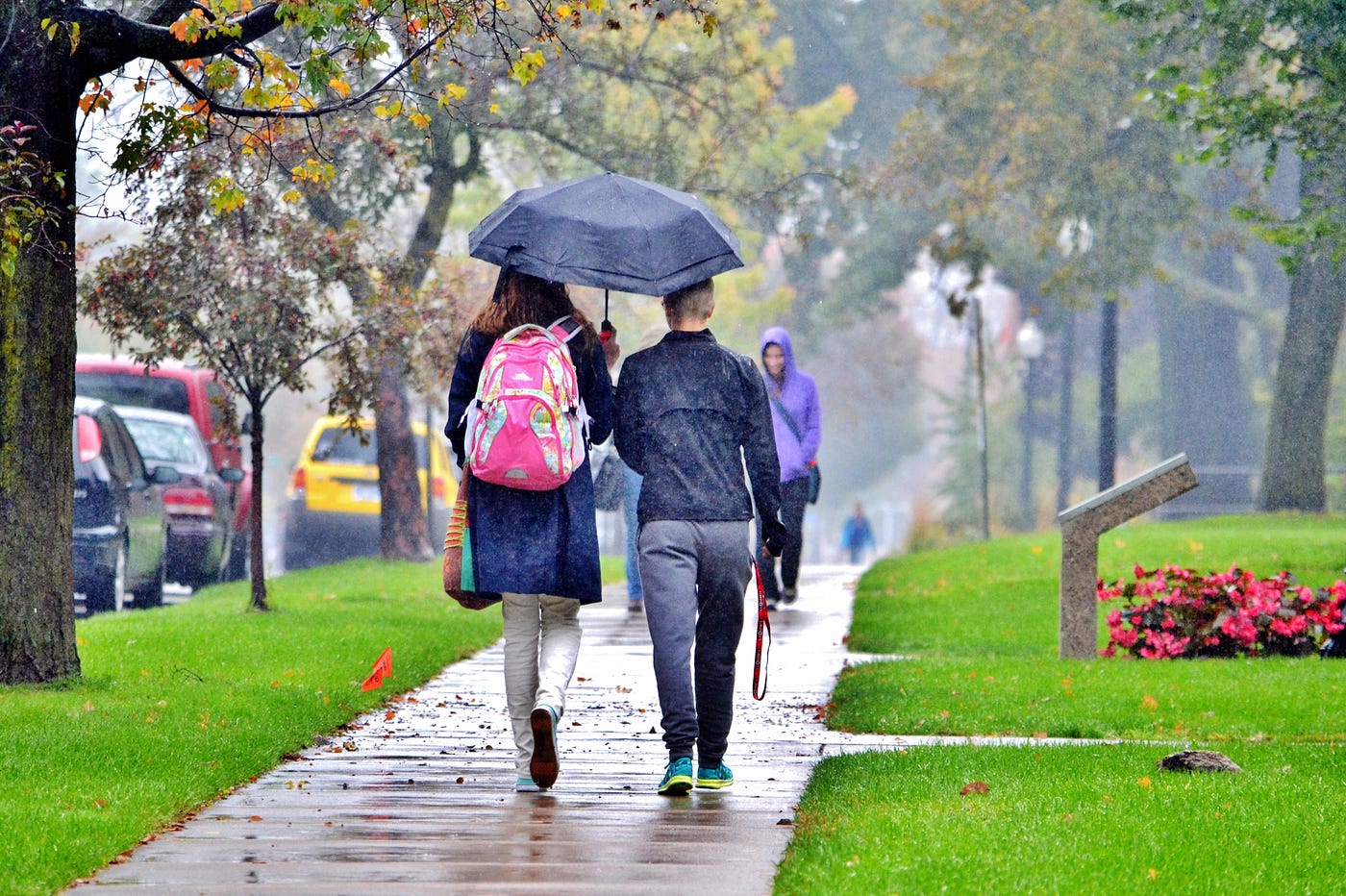 Two students share an umbrella while walking along a wet sidewalk.